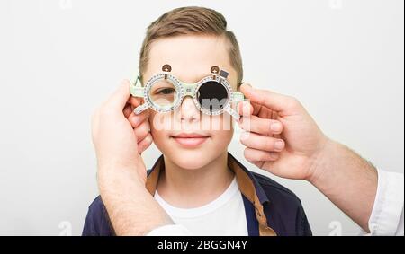 Optometriker setzt auf den Jungen spezielle Brille, um die Sehschärfe wiederherzustellen. Amblyopie-Behandlung in einer ophthalmologischen Klinik Stockfoto