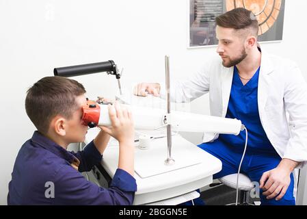 Junge Blick in Gerät, um die Vision zu stimulieren. Augenarzt Überwachung der Behandlung der Sehschärfe mit pleoptischen Methoden. . Augentraining Stockfoto