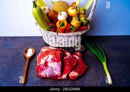 Korb voll mit Gemüse und Wurzeln hinter rohem Fleisch Stockfoto