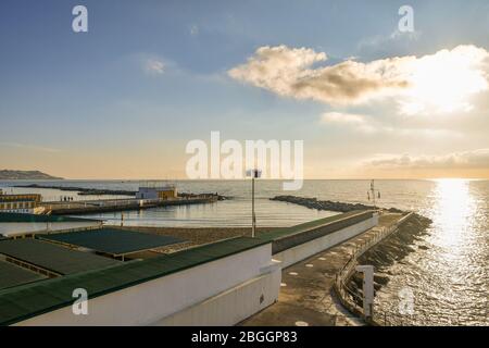 Hohe Winkel, Hintergrundbeleuchtung Blick auf eine Küste mit einem Pier und die Strandhütten eines Badehauses bei Sonnenuntergang, Sanremo, Imperia, Ligurien, Italien Stockfoto