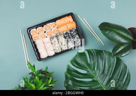 Japanisches Essen. Sushi mit Essstäbchen, auf grünem Hintergrund mit tropischen Blättern im Take Away. Draufsicht. Stockfoto