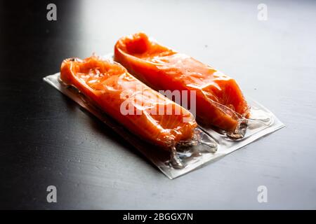 Roter Fisch oder Lachsfilets in Vakuumverpackung auf schwarzem Hintergrund. Frischer Fisch. Omega-3. Nahaufnahme. Selektiver Fokus. Stockfoto