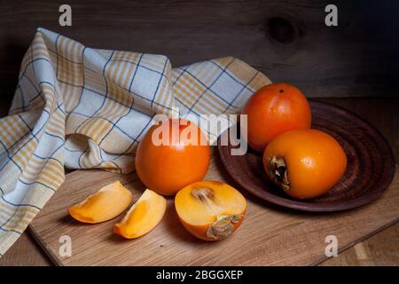 Zusammensetzung aus reifen, köstlichen ganzen persimonischen Früchten, halbierten und geschnittenen Früchten, die auf Holzgrund verzehrt werden können. Stockfoto