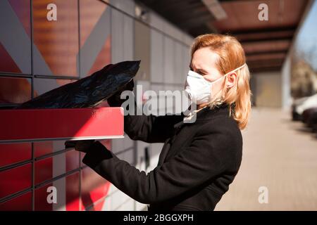 dame, die eine Gesichtsmaske trägt, erhält ein Paket oder Paket von einem Postpaket-Terminal in Tallinn. Frau, die eine Gesichtsmaske trägt, schützt vor Stockfoto