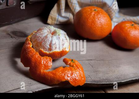 Mehrere ganz frische orangefarbene Mandarinen oder Orangen, Tangerinen, Clementinen, Zitrusfrüchte und eine Frucht sind halb auf Holzbrett geschält Stockfoto