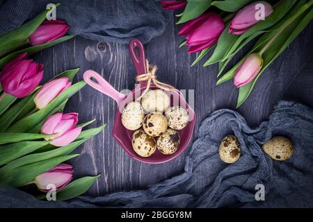 Gefleckte Wachteleier und Frühlingsblumen Tulpen auf einem grauen Holzhintergrund. Draufsicht Stockfoto