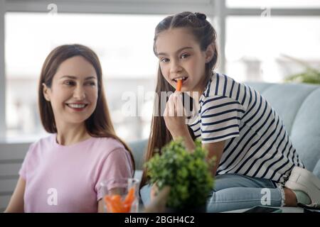 Mama schaut ihre Tochter an, die eine Karotte isst. Stockfoto