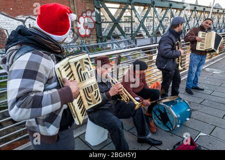 Gruppe von Musikern, die draußen buschieren. Busker spielen Musik auf Akkordeons, Trompeten und einer Trommel auf einer Brücke, London, England, Großbritannien Stockfoto