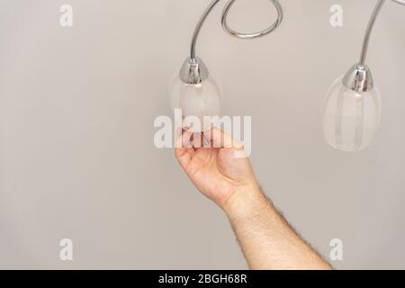 Die Hand eines Mannes dreht eine Glühbirne aus einem Lampenschirm. Lampenaustausch Stockfoto