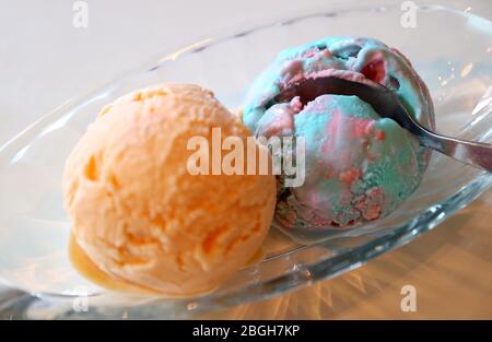 Nahaufnahme Löffel aufschaufeln Bubble Gum Ice Cream mit verschwommener Orange Ice Cream im Vordergrund Stockfoto