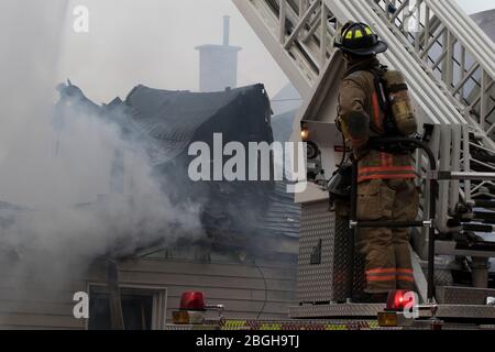 Ontario, Kanada April 20 2020: Rauchen Haus auf Feuer mit extremen Schäden. Feuerwehrleute gießen Wasser, um das Feuer aus einem großen Hausbrand zu löschen. depa feuern Stockfoto