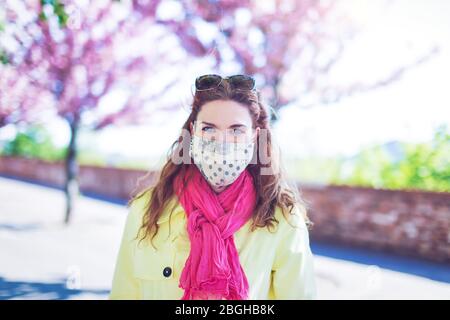 Junge modische Frau Porträt in Maske im Park während Sakura Stockfoto