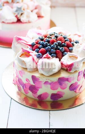 Weißer und rosa Birhday Kuchen mit Baiser und frischen Beeren, Himbeeren, Erdbeeren und Heidelbeeren. Weißer Holzhintergrund. Stockfoto