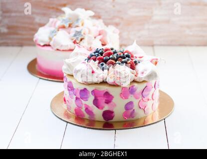 Weißer und rosa Birhday Kuchen mit Baiser und frischen Beeren, Himbeeren, Erdbeeren und Heidelbeeren. Weißer Holzhintergrund. Stockfoto