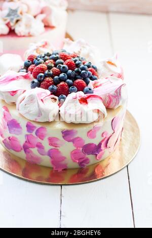 Weißer und rosa Birhday Kuchen mit Baiser und frischen Beeren, Himbeeren, Erdbeeren und Heidelbeeren. Weißer Holzhintergrund. Stockfoto