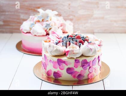 Weißer und rosa Birhday Kuchen mit Baiser und frischen Beeren, Himbeeren, Erdbeeren und Heidelbeeren. Weißer Holzhintergrund. Stockfoto