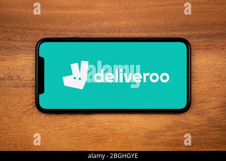 Ein Smartphone mit dem Deliveroo-Logo liegt auf einem einfachen Holztisch (nur für redaktionelle Verwendung). Stockfoto