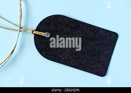 Schwarzer, abgerundeter Geschenkanhänger mit Naturjutebinden. Kraft Karton Etikett auf hellblauem Hintergrund mit Kopierfläche. Stockfoto
