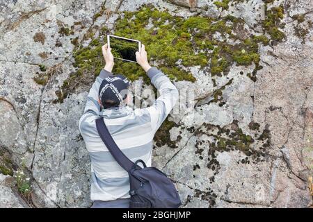 ZAPORIZHZHYA, UKRAINE - 28. JUNI 2018: Ein Mann, der Moos auf einem Felsen mit einem Tablet während des PhotoCamp fotografiert Ukrainische Fotografen Jahrestreffen o Stockfoto