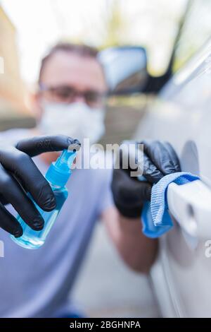 Fahrer mit Gesichtsmaske trägt Gummischutzhandschuhe wischen und sprühen Autotür Griff. Konzept zur Virus- und Bakterienprävention. Stockfoto