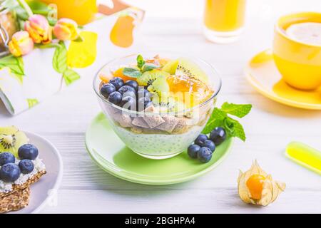 Joghurt mit Chiasamen, Maispflaumen, Kiwi, Heidelbeeren, Physalis und Minze auf weißem Holzhintergrund Stockfoto