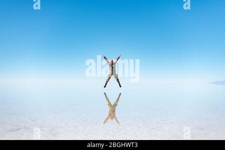 Mann springt in Salar de Uyuni, Salt Flats Uyuni, Südwest-Bolivien während der Regenzeit (nass), wenn Salzebenen überflutet werden und eine Spiegelreflexion ermöglichen. Stockfoto