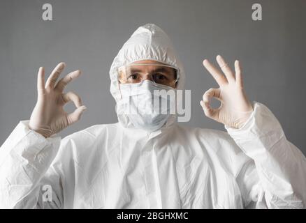 Arzt in weißem Schutzanzug, medizinischer Maske und Gummihandschuhen zeigt, dass alles in Ordnung ist. Hilfe für Menschen während der Bedrohung durch Coronavirus durch Pandemie Stockfoto