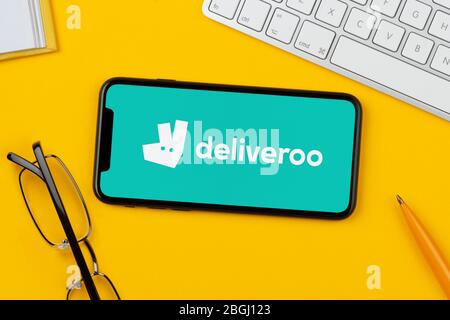Ein Smartphone mit dem Deliveroo-Logo liegt auf einem gelben Hintergrund zusammen mit Tastatur, Brille, Stift und Buch (nur zur redaktionellen Verwendung). Stockfoto