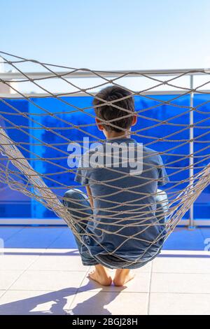 Traurig enttäuscht, müde Kind allein in Hängematte auf dem Balkon an sonnigen Tag sitzen Stockfoto