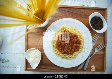 Spaghetti Bolognese mit Hackfleisch, Zwiebel, gehackte Tomaten, Tomatenmark . Rohe Spaghetti-Pasta in einer Schüssel. Schwarzer Pfeffer, Mayonnaise in einer Schüssel Stockfoto