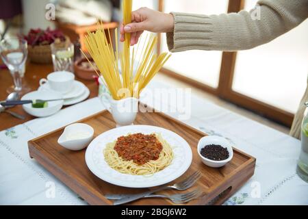 Spaghetti Bolognese mit Hackfleisch, Zwiebel, gehackte Tomaten, Tomatenmark . Rohe Spaghetti-Pasta in einer Schüssel. Schwarzer Pfeffer, Mayonnaise in einer Schüssel Stockfoto