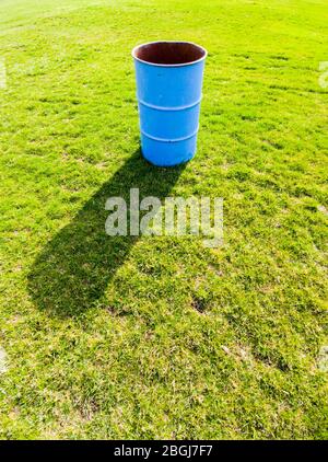 Einzelne blaue Metallbehälter werfen Schatten auf grünes Grasfeld. Stockfoto