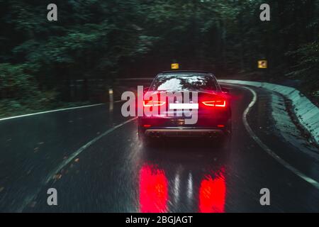 Fahren Sie mit dem Auto auf der regnerischen Straße mit roten Xenon-Lichtern Stockfoto