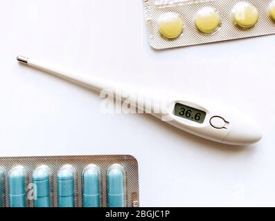 Elektronisches Thermometer und Pillen auf weißem Hintergrund. Medizin und Gesundheitskonzept.Behandlung von Viruserkrankungen. Stockfoto