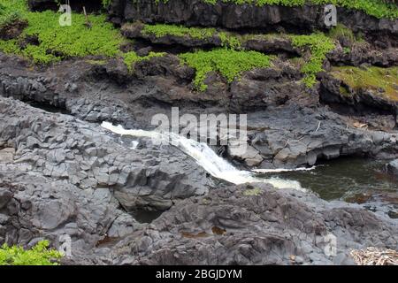 Ein Abschnitt des Palikea Stream, Oheo Gulch, Seven Sacred Pools, der durch Vulkangestein mit Scaevola Taccada Pflanzen läuft, die im Felsen wachsen, Maui, Hawa Stockfoto
