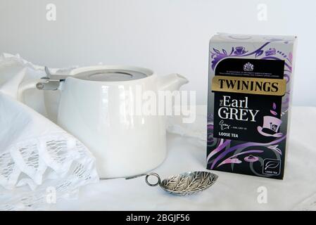 Twining's Earl Grey loser Tee im Paket mit weißer Teekanne und Teeblätterlöffel auf weißer Spitzenserviette Stockfoto