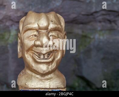 Fengdu, China - 8. Mai 2010: Geisterstadt, historisches Heiligtum. Nahaufnahme des goldenen Kopfes des Mannes lächelnd mit 2 Zähnen vor schwarzer Kulisse. Stockfoto