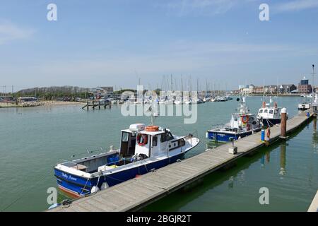 Kleine Boote, die am Gehweg im Hafen von Littlehampton in West Sussex, Großbritannien, mit den Yachten des Arun Yacht Club in der Ferne anhegen Stockfoto