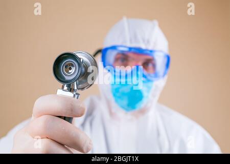 Stethoskop in männliche Ärzte Hand in weißen Schutzanzug und Maske isoliert. Selektiver Fokus, Stockfoto