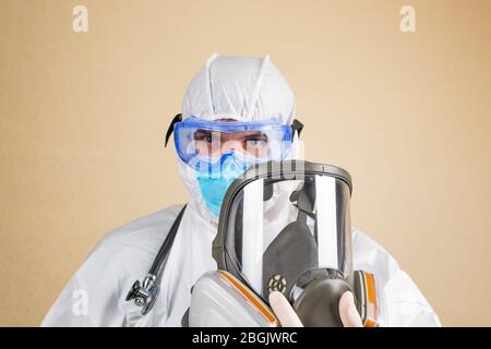 Arzt trägt weißen Schutzanzug und Stethoskop voll Gesicht Atemmaske in der Hand isoliert. Selektiver Fokus. Stockfoto