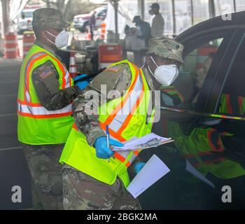 New York Army National Guard Spc. Shevon Reid wurde neben SPC der 107. Militärpolizei Company, dem 53. Truppenkommando, der New Yorker Armee-Nationalgarde zugewiesen. Jason Trinadad, 369th Sustainment Brigade HHC, 53. Truppenkommando, gibt den Leuten Anweisungen in einem COVID-19 Mobile Testing Center im Glenn Island Park, New Rochelle, April. 4, 2020. Die New York National Guard unterstützt weiterhin sieben Drive-Thru-Teststandorte. Soldaten und Luftwaffe sammeln Proben und bieten allgemeine Unterstützung an den Teststandorten an, die insgesamt 5,000 Tests pro Tag übersteigen. (USA Nationalgarde Der Armee Stockfoto