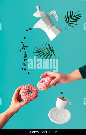 Levitation surrealistischen Bild, Kaffee und zwei rosa Donuts in den Händen. Fliegende Kaffeebohnen. Keramik-Kaffeemaschine und Espresso-Tasse. Lebendig, trendig, auffällig Stockfoto