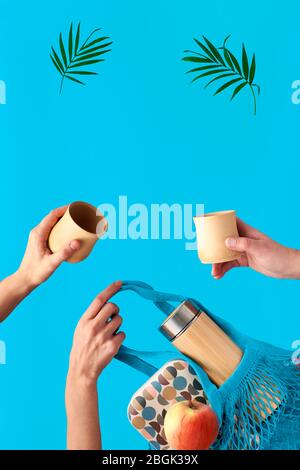 Drei Hände mit Tasse und Palmblatt, Netzbeutel mit Lunchbox und Teeflasche fliegen. Kein Abfall des Tees in einem umweltfreundlichen isolierten Bambuskolben. Keine Verschwendung Stockfoto