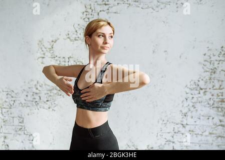 Schönes junges Mädchen geht in für Sport zu Hause in einer Sportuniform auf einem Teppich. Die süße Blondine ist auf einem Hintergrund einer weißen Ziegelwand in Fitness engagiert. Stockfoto