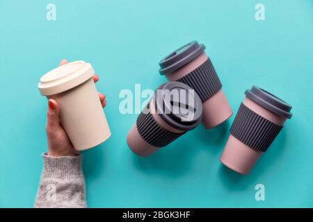 Verschiedene Bambus Reise wiederverwendbare Kaffee oder Tee Tassen oder Maden mit Silikon Isolierung.Hände öffnen Silikon-Deckel. Flaches Lay, blauer Papierhintergrund. Öko-Kühlschrank Stockfoto