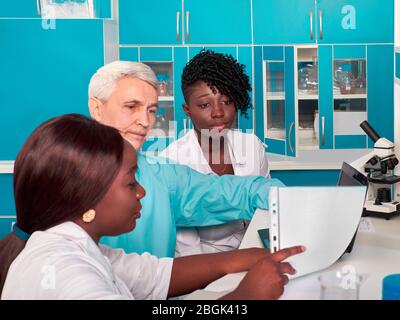 Fortschrittsbericht im Testlabor. Afrikanische Medizinstudenten, Absolventen zeigen Daten für kaukasischen Mann, Senor wissenschaftlicher Berater. Blut ausführen, pcr Stockfoto