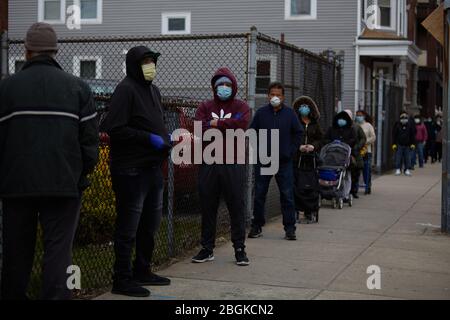 Chelsea, Massachusetts, USA. April 2020. Die Bewohner warten in der Schlange, um Lebensmittelkisten und warme Mahlzeiten zu sammeln. Die COVID-19, Corona Virus, Situation in Chelsea, Massachusetts ist ein wichtiger Hotspot. Chelsea ist die am stärksten getroffenen Städte im Bundesstaat. Chelsea ist eine lateinamerikanische Einwandererbevölkerung mit 80% der Bevölkerung sind wichtige Arbeitskräfte, wie Lebensmittelarbeiter. Mit verlorenen Jobs haben Leute eine harte Zeit, in der Lage zu sein, Nahrung zu erhalten. Die Heilsarmee gibt täglich Lebensmittelboxen und warme Mahlzeiten aus. Linien streckt für Stadtblöcke, um Lebensmittelboxen zu bekommen. Kredit: Allison Dinner/ZUMA Wire/Alamy Live News Stockfoto