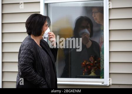 Chelsea, Massachusetts, USA. April 2020. Eine Frau besucht ihre Mutter am Fenster ihres Pflegeheims. Die COVID-19, Corona Virus, Situation in Chelsea, Massachusetts ist ein wichtiger Hotspot. Chelsea ist die am stärksten getroffenen Städte im Bundesstaat. Chelsea ist eine lateinamerikanische Einwandererbevölkerung mit 80% der Bevölkerung sind wichtige Arbeitskräfte, wie Lebensmittelarbeiter. Mit verlorenen Jobs haben Leute eine harte Zeit, in der Lage zu sein, Nahrung zu erhalten. Kredit: Allison Dinner/ZUMA Wire/Alamy Live News Stockfoto