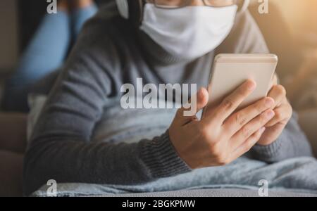 Junge Frau mit Maske zu Hause bleiben Musik mit Smartphone hören, Kopfhörer entspannende Emotion. Verhindern Sie die Ausbreitung von Coronavirus Quarantäne. Stockfoto