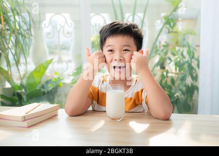 Ein asiatischer Junge, der Milch trinkt, während er am Schreibtisch sitzt, nachdem er Hausaufgaben gemacht hat. E-Learning und Bildungskonzept. Stockfoto